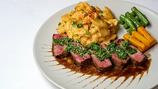 Reverse seared steak with garnish and sauce, served with mac and cheese and vegetable sides